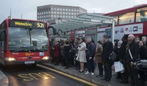 commuters in a grey london street queuing for a bus