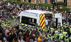 immigration van and police surrounded by a crowd. The man in the van is thanking the crowd for turning out and securing his release