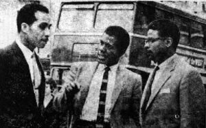 three men talking, with a bus in the background - from the bus boycott