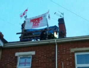 eviction resisters on the roof of a house, with banner "homes for all"