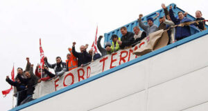 workers from one of the Visteon occupations, on the roof of their factory with the banner "Ford terms"